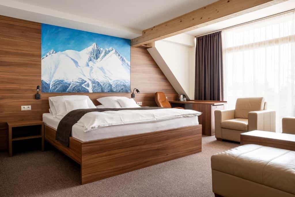 Hotel room with wooden accents, white bedding, and a large painting of snowy mountains.