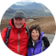 Hikers smiling in red and purple jackets with mountains and glacier in background