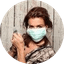 Woman wearing a light blue face mask against a wooden background.