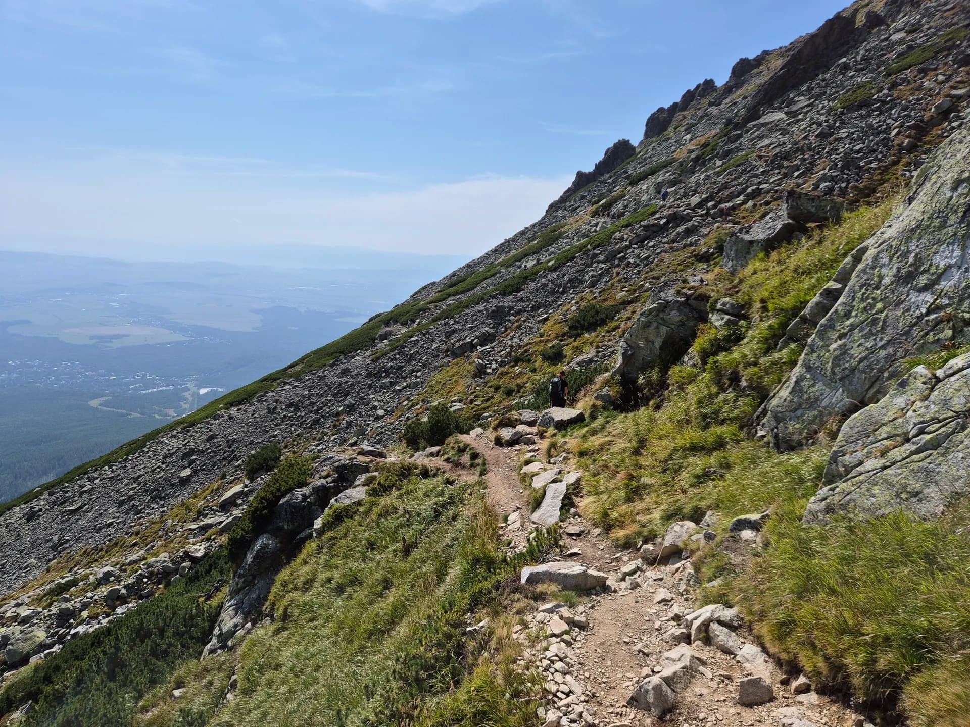 Hiker on a rocky mountain trail in the Tatra Mountains with a view of the valley below.