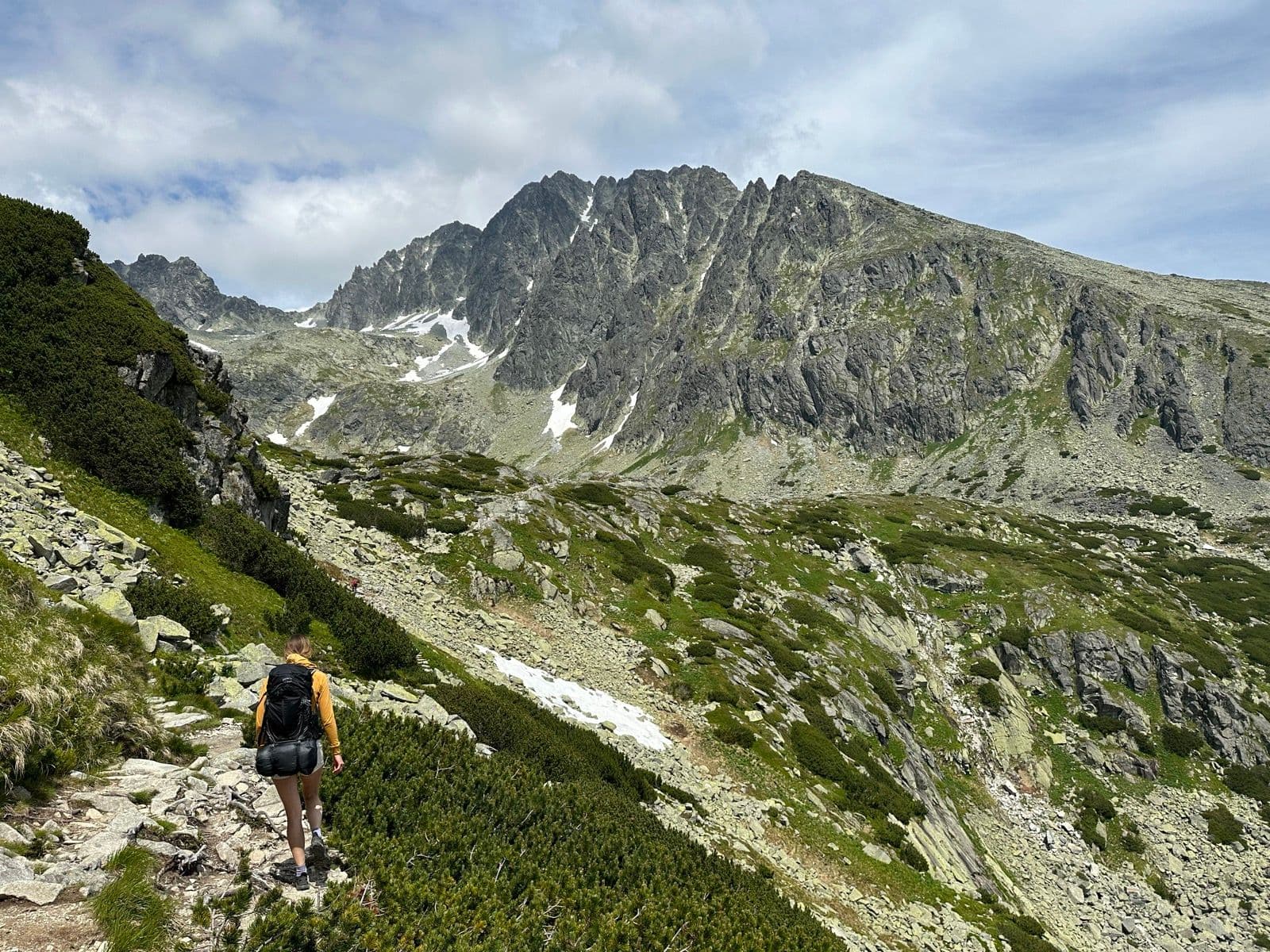 Hiker with a backpack walking on a rocky mountain trail in the High Tatras.