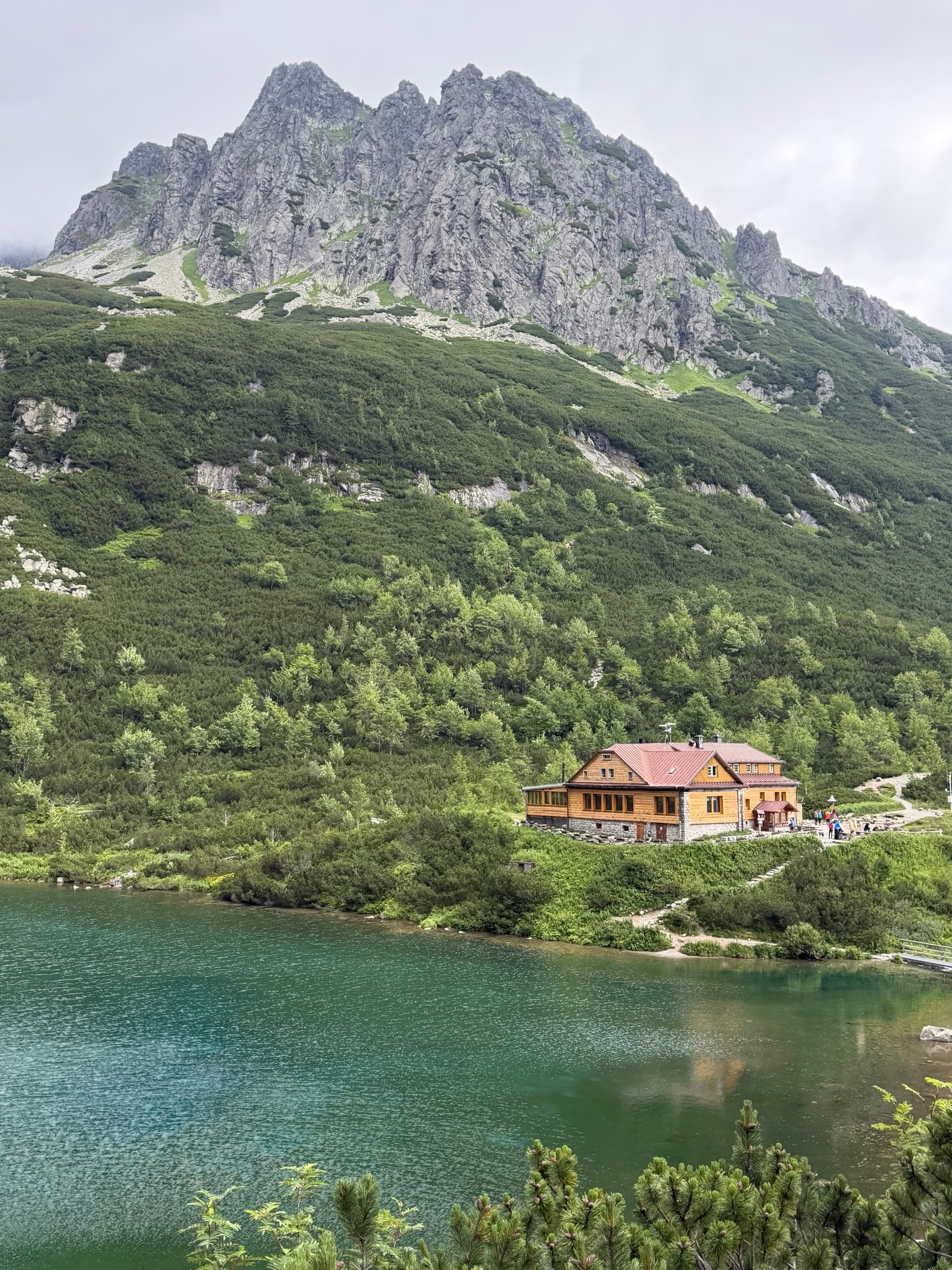 Wooden hut by green alpine lake below rocky mountain peaks