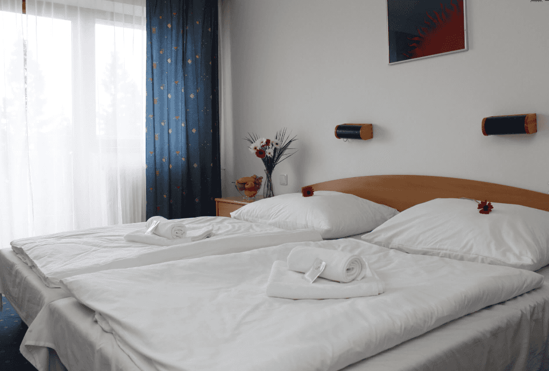Twin beds with crisp white linens, rolled towels, and flowers in a bright hotel room.