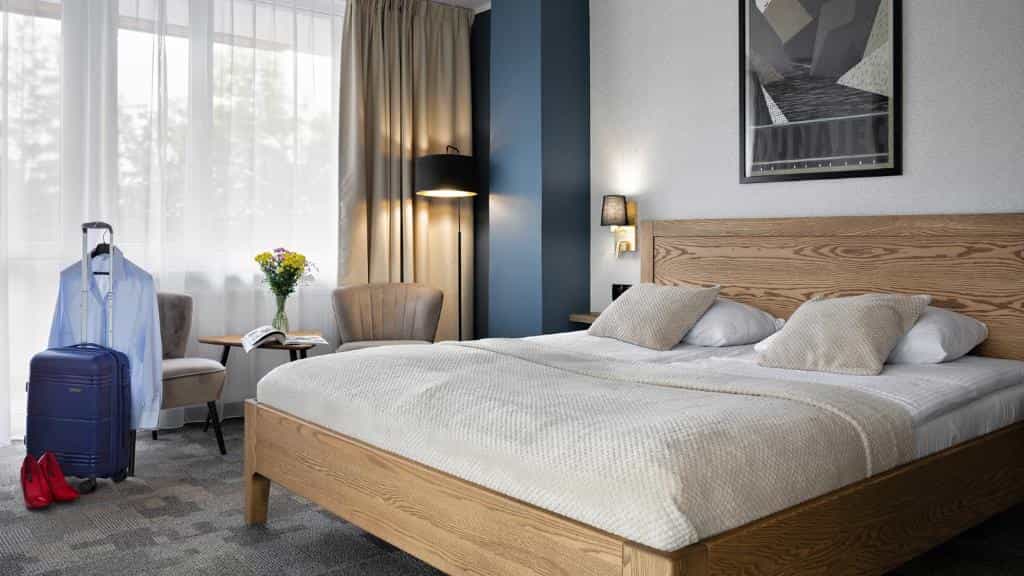 Hotel Rzemieślnik Zakopane hotel room with wooden bed, blue suitcase, and natural light.