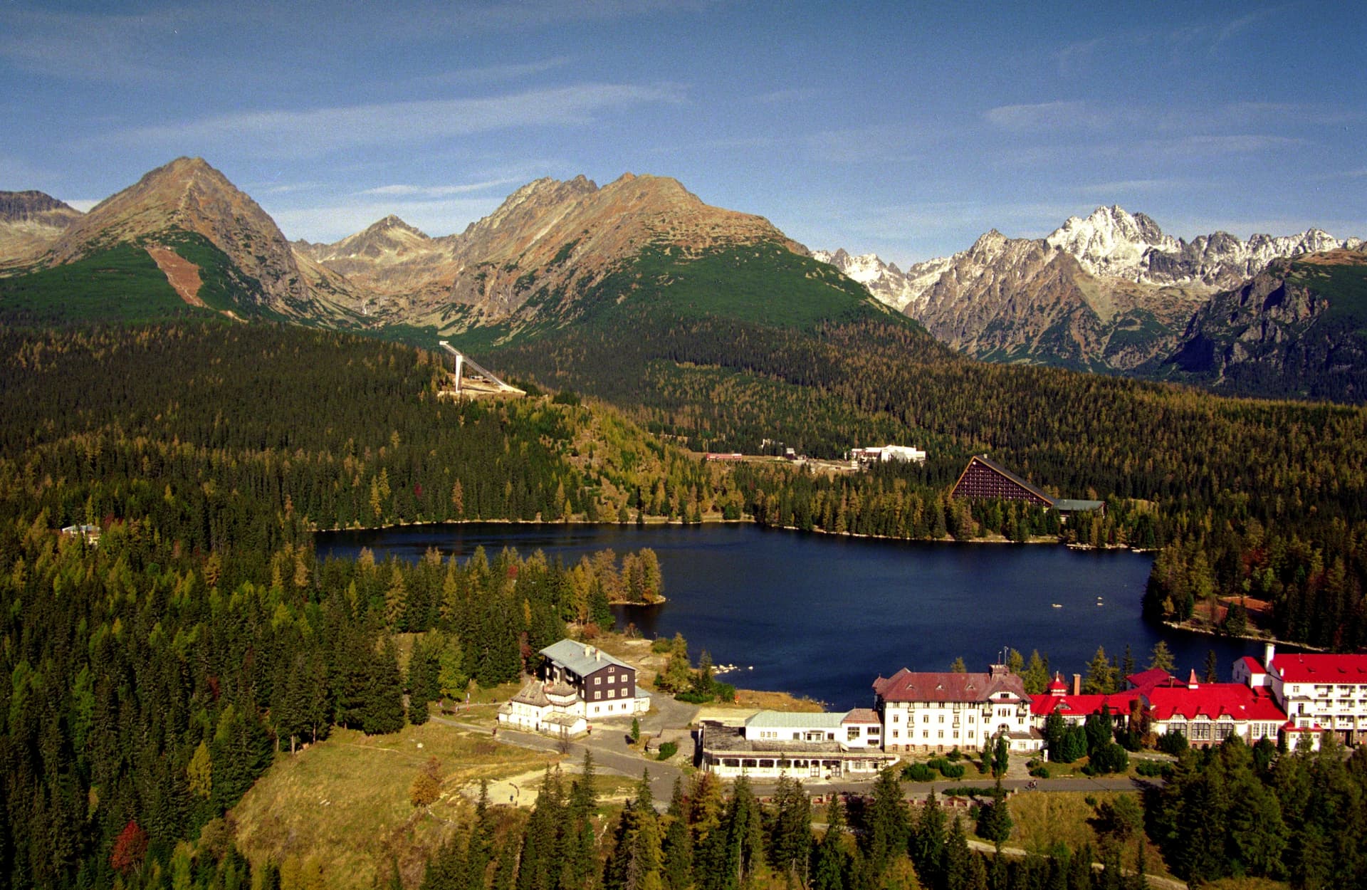 Buildings and lake at Štrbské Pleso surrounded by dense forest and rugged mountains.